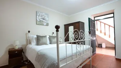 a white bedroom with a bed and a staircase at Marroas Cottage in Ponta do Sol