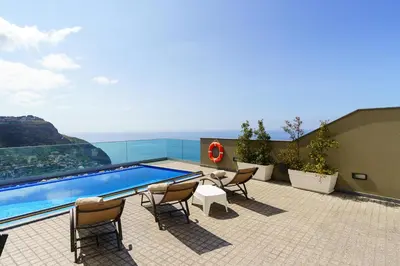 a patio with chairs and a swimming pool on a building at Villa António in Arco da Calheta