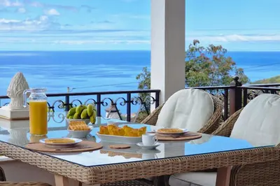 a wicker chair and a glass of orange juice on a table at Villa Branca in Ponta do Sol
