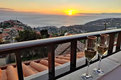 two glasses of wine on a balcony with the sunset at Villa Branca in Ponta do Sol