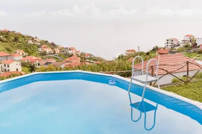a blue swimming pool with a chair in front of a house at Casa do Vale by Mth in Ribeira Brava