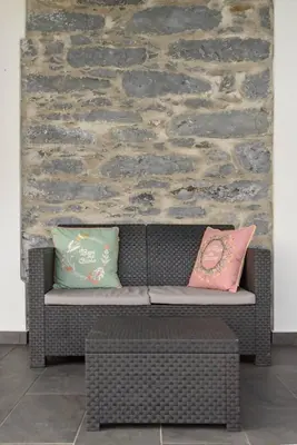 a wicker couch with two pillows in front of a stone wall at Casa do Vale by Mth in Ribeira Brava
