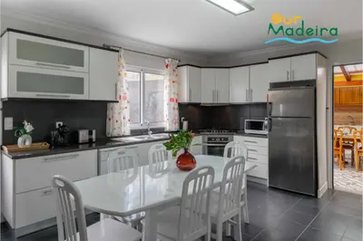 a kitchen with white cabinets and a white table and chairs at OurMadeira - Yellow House in Raposeira do Logarinho