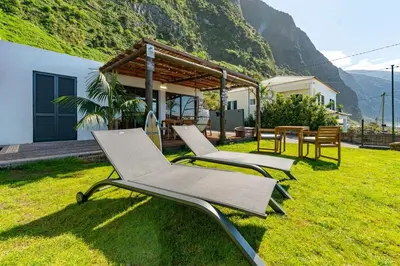 a group of chairs sitting on the grass in front of a house at Fajã Lodges - House Ash in São Vicente