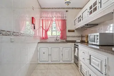 a kitchen with white cabinets and a window with pink curtains at Valley Nest by Zest and Guest in Ribeira Brava