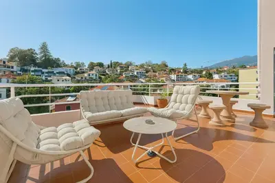 a balcony with white chairs and a table and a city at Perla do Oceano - Funchal Sea View with XL Terrace in Funchal