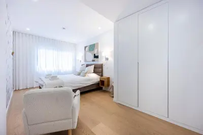 a white bedroom with a bed and a chair at Paraíso Florido by the sea in Luz