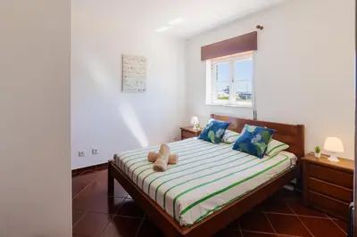 a bedroom with a bed with blue pillows and a window at Sunny House in Sagres