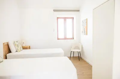 a white room with two beds and a chair at Green House Beach Side Oasis in Vila Baleira