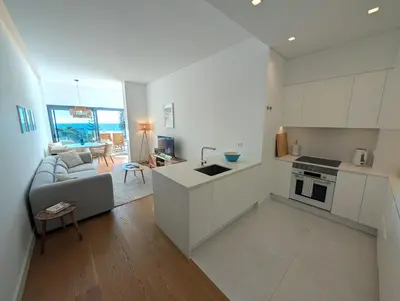 a kitchen and living room with white cabinets and a couch at Breathtaking Oceanfront Living, Sunset Facing 3-Bedroom Flat in Acqua Residences in Funchal