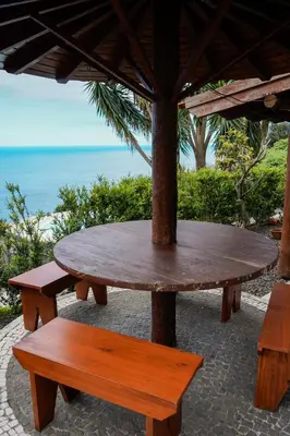 a wooden table and two benches under an umbrella at Refúgio do Norte in Porto Moniz