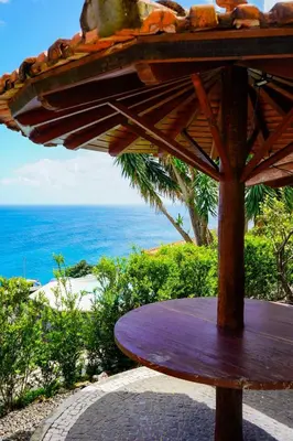 a wooden table with an umbrella in front of the ocean at Refúgio do Norte in Porto Moniz