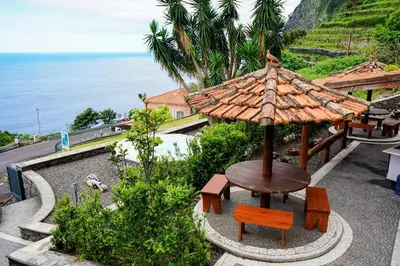 a table and chairs with an umbrella and the ocean at Refúgio do Norte in Porto Moniz