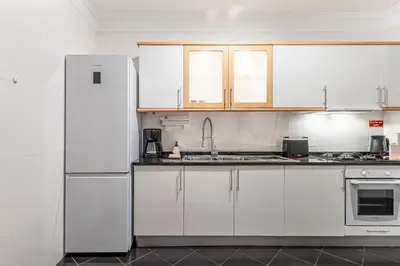 a kitchen with white cabinets and a white refrigerator at Bright Modern 2BR Apartment Near Cristo Rei in Caniço