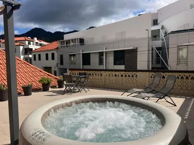 a hot tub on a patio with chairs and a building at Casa do Ribeirinho in Machico