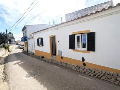 a white building with black shuttered windows on a street at Casinha da Raposeira in Raposeira