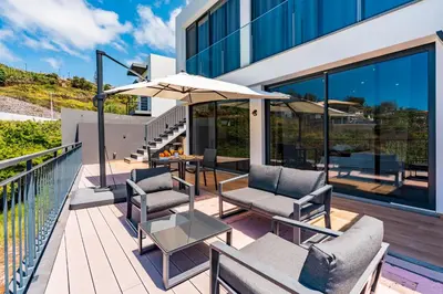 an outdoor deck with chairs and an umbrella at Casa Branca-B,beautiful sea view in Estreito da Calheta