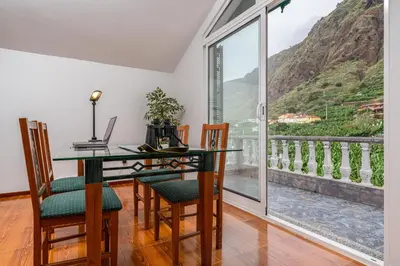 a dining room with a table and chairs and a balcony at Casa Carreiro in Paul do Mar