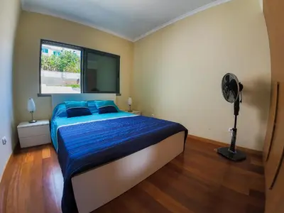 a bedroom with a bed with blue sheets and a fan at Moradia Garcês in Santa Cruz