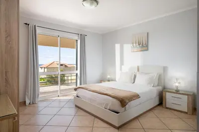 a white bedroom with a bed and a large window at Gazela House Comfort & Barbecue in Porto Santo in Porto Santo