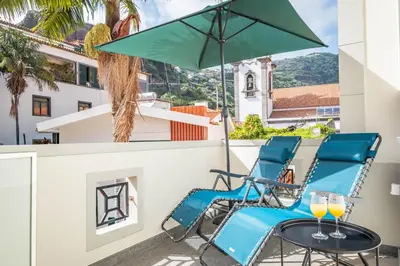 a pair of blue chairs and an umbrella on a balcony at Nati by KAAMAH in Ribeira Brava