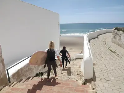 two people walking up a staircase with a surfboard at Burgau Ocean View Apartment in Burgau