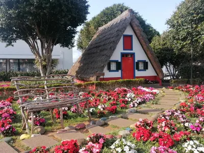 a small house with a thatched roof and flowers at House Vila Santa Ana in Santana