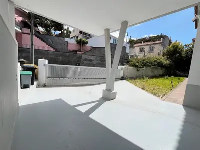 a woman sitting at a table on a balcony with an umbrella at Sunny Double Room in 4BR Villa with AC, Sea View Balcony, Workspace in Funchal