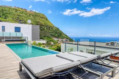 a pool with lounge chairs and the ocean in the background at Villa Arco-Iris, a Home in Madeira in Arco da Calheta