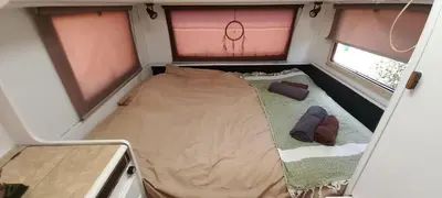 a small bed in the middle of a room with two windows at Pauls caravan for 4 - See the horses from your bed in Barão de São João