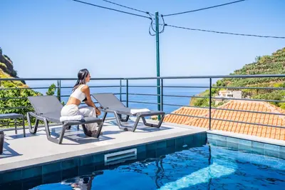 a woman sitting on a chair next to a swimming pool at Atlantic Pebble Villa in Ribeira Brava