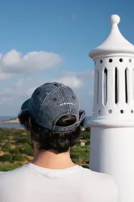 a man wearing a hat standing next to a white lighthouse at Outsite Sagres - Work, Connect, Explore in Sagres