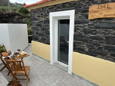 a door to a stone building with a table and a chair at Refúgio do Nevoeiro Apart T1 in Porto Moniz