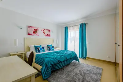 a bedroom with a bed and a window with blue curtains at Casa Maria at Boavista Resort Lagos in Atalaia