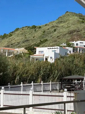 a white fence in front of a hill with houses at A casa da Xã in Almagreira