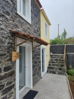 a retaining wall with plants and a house in the background at Refúgio do Nevoeiro Estudio in Porto Moniz