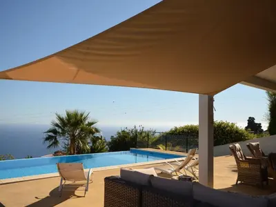 a patio with chairs and a swimming pool with an umbrella at Villa 17°West with Pool in Estreito da Calheta