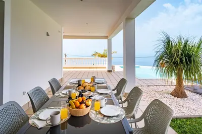a dining room with a table and chairs and the ocean at Quinta dos Louros in Estreito da Calheta