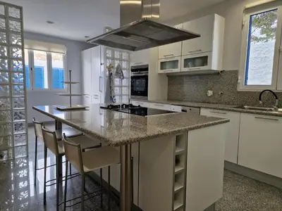 a kitchen with white cabinets and a island with bar stools at L'Oasis Palm Beach House in Porto Santo