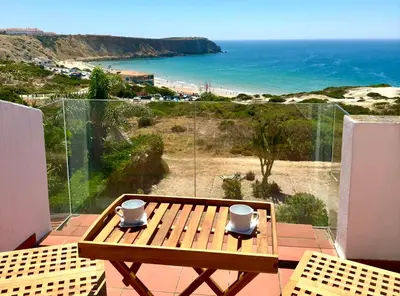 a wooden table on a balcony with a view of the beach at Casa Mareta in Sagres