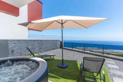 a hot tub with an umbrella and chairs on a balcony at Blue Outlook Retreat by Atlantic Holiday in Água de Pena