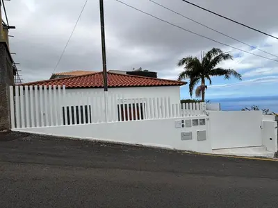 a white fence in front of a house with a palm tree at Casa Ribeiro in Funchal
