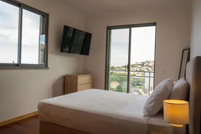a bedroom with a bed and a tv and windows at Casa da Baía Overlooking Funchal Bay in Funchal