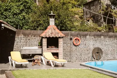 a patio with two chairs and a fireplace next to a pool at Casa da Pedra by Amazing Madeira in Santana