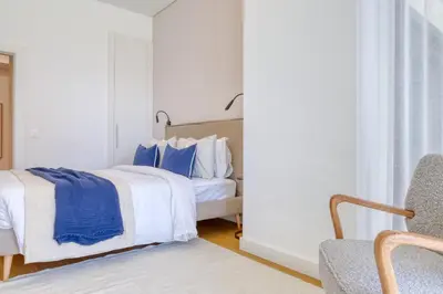 a white bedroom with a bed and a chair at Funchal Acqua Blue 3H, a Home in Madeira in Funchal