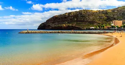 a beach with people on the water and a mountain at Paraíso Altântico in Machico