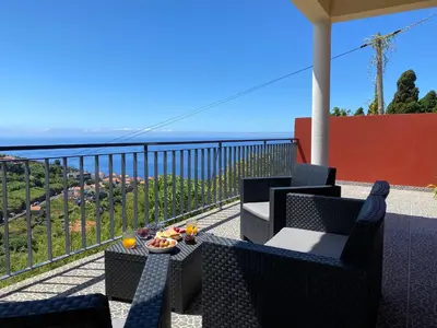 a balcony with chairs and a table with a view of the ocean at Rocha House in Calheta