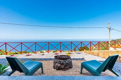 two chairs and a tree stump with the ocean in the background at Casa D'Avó Bela in Arco da Calheta