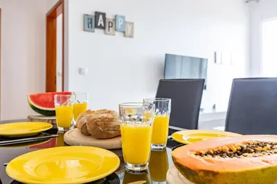 a table topped with yellow plates and glasses of orange juice at Pérola Apartments by YOUR KEY in Caniço