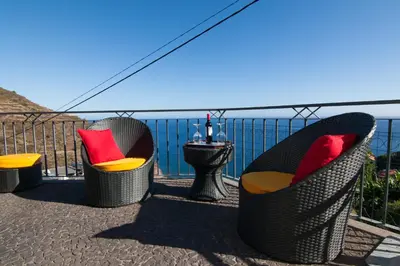 three chairs and a table on a balcony overlooking the water at Casa Nici in Calheta